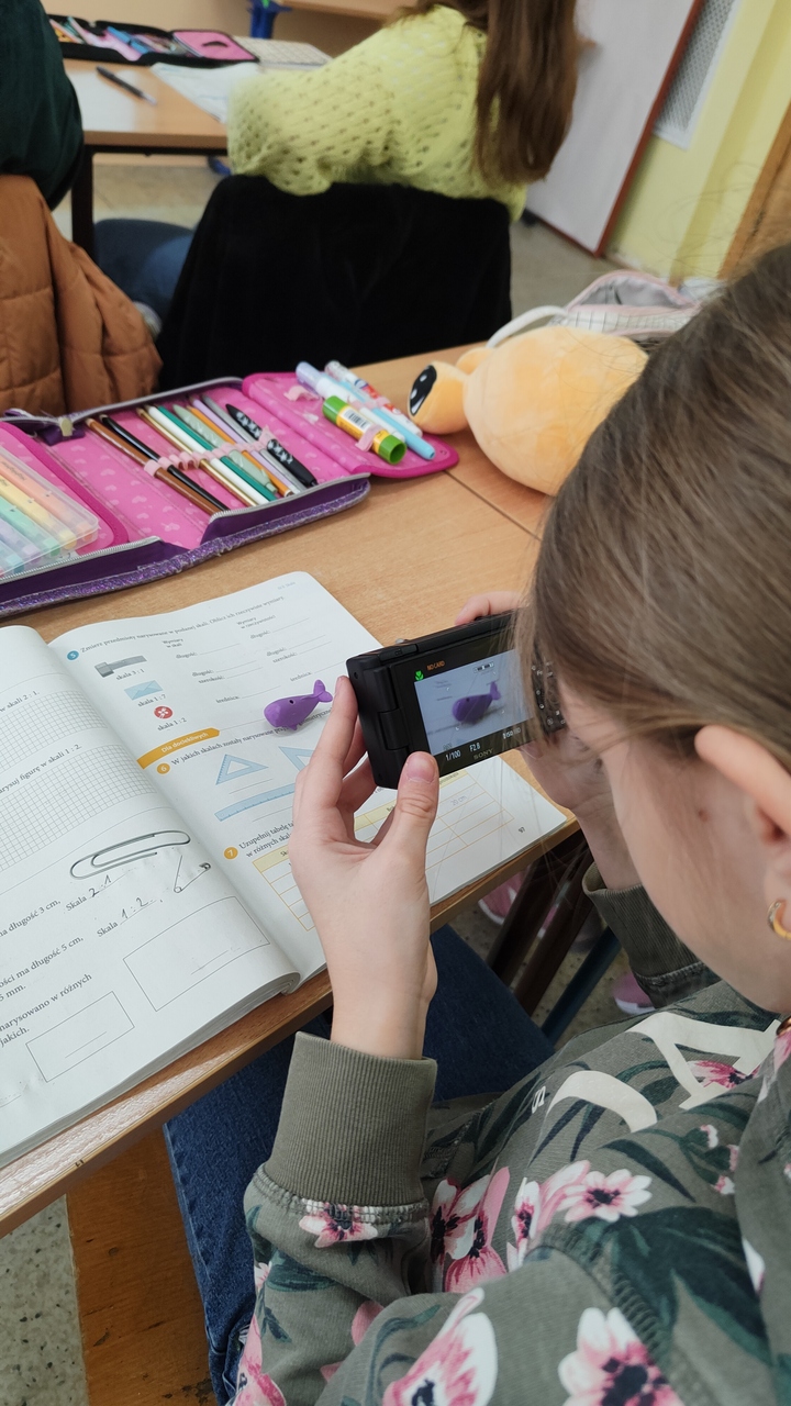 dziewczynka robi zdjęcie fioletowego wielorybka na książce od matematyki